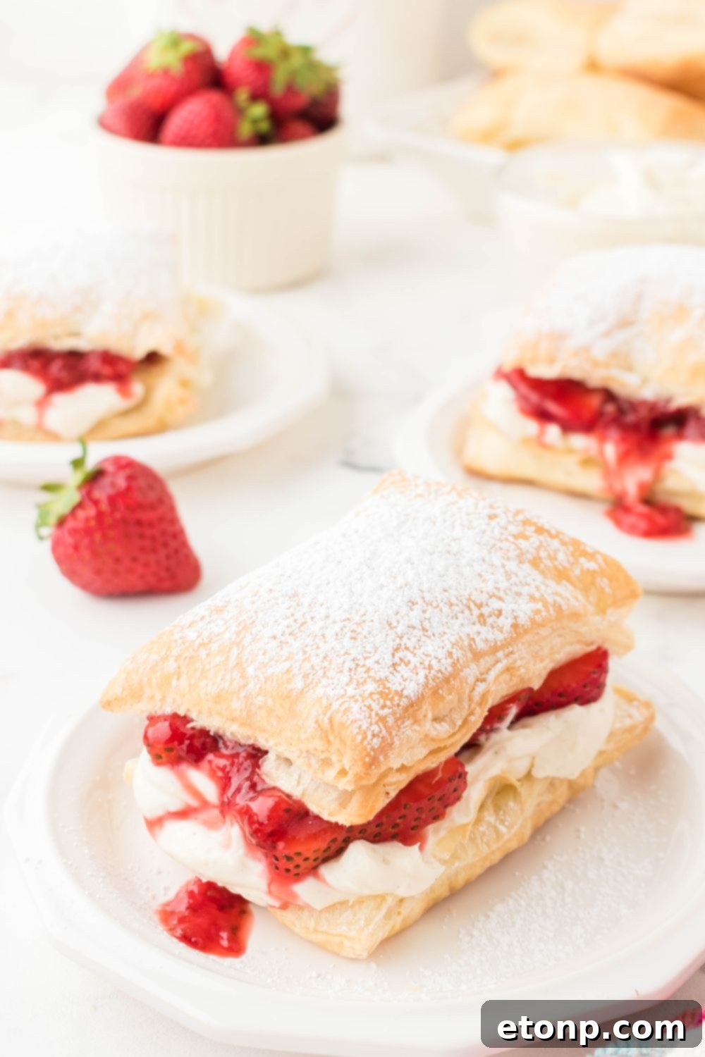 A spread of individual strawberry puff pastry desserts on plates scattered across a table, ready for guests to enjoy.