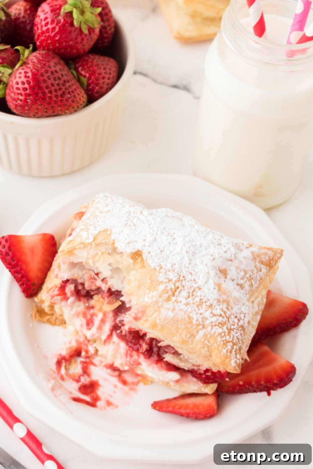 A Strawberry Puff Pastry with a bite taken out, revealing the delightful layers of flaky pastry, creamy filling, and fresh strawberries within.