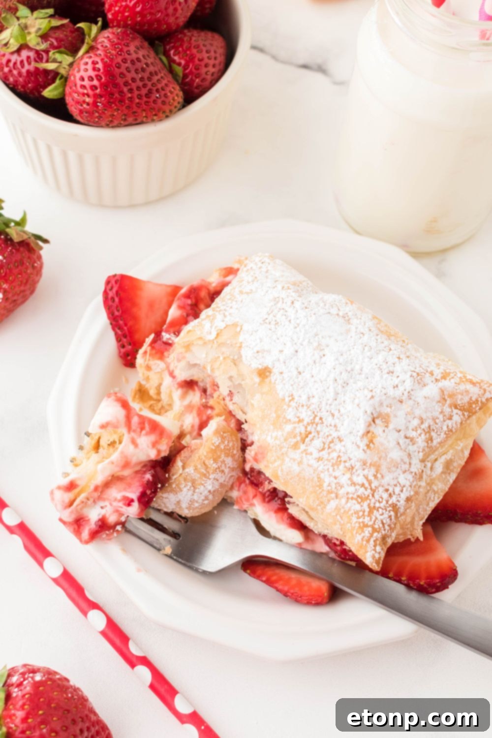 A close-up of a fork resting on a plate with a Strawberry Flaky Puff, inviting a delicious bite.