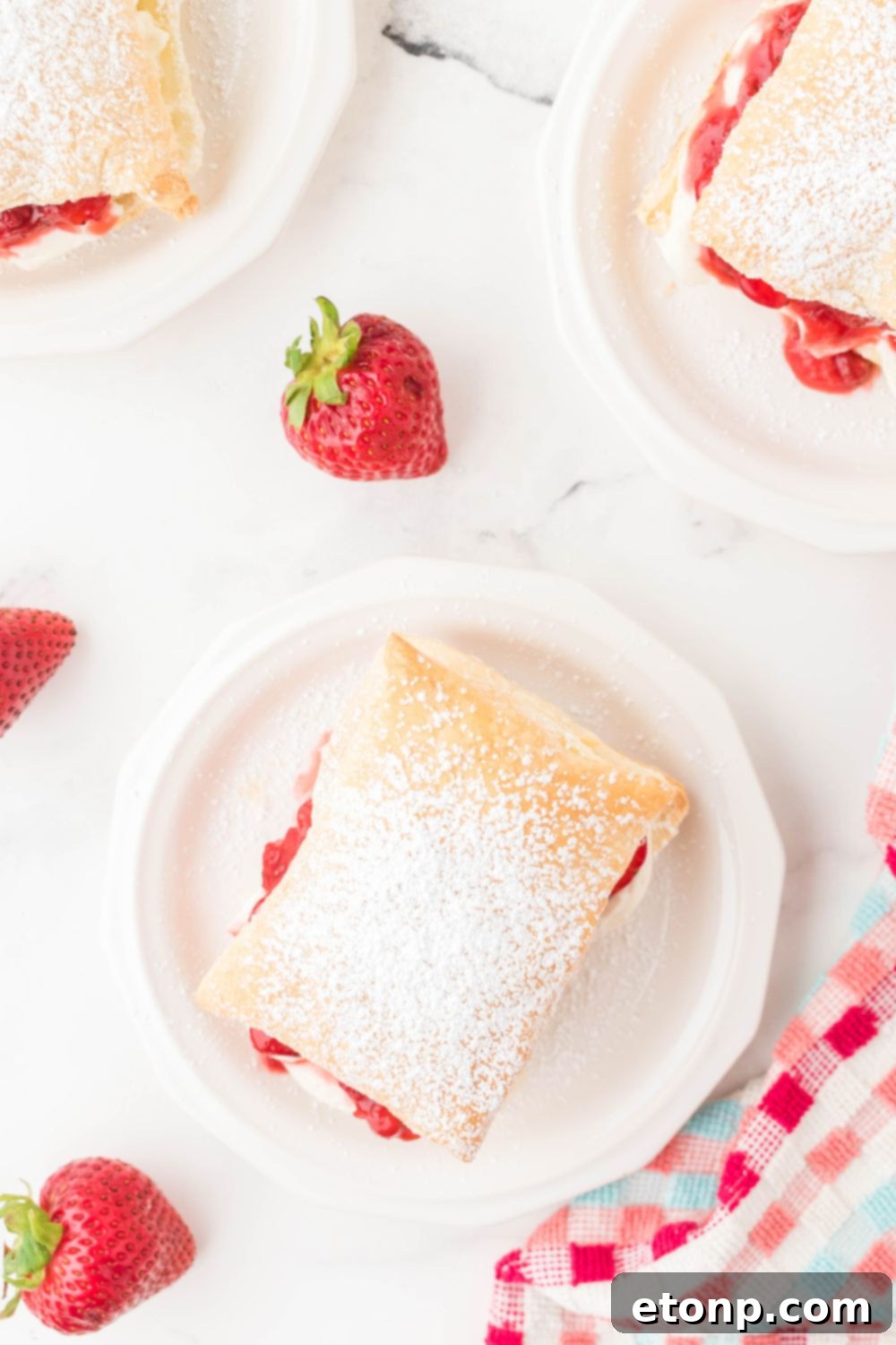 Multiple strawberry puff pastries arranged on plates, surrounded by fresh berries on a dining table, creating a picturesque dessert display.