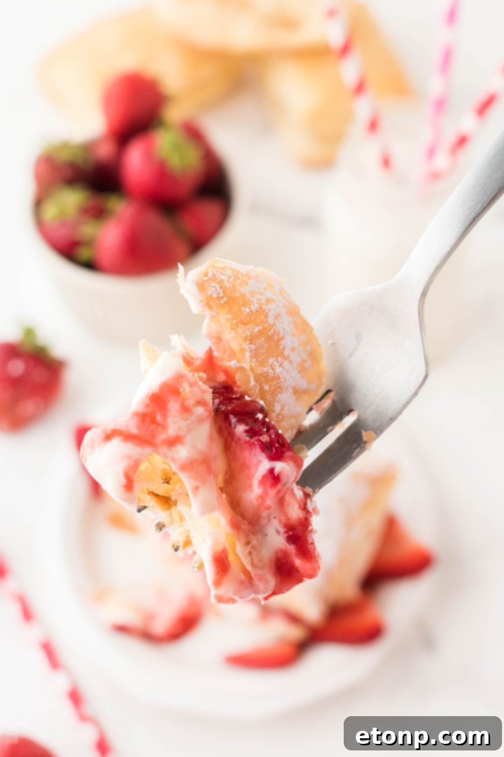 A fork holding a piece of strawberry puff pastry, showing off its interior layers of fruit and cream, ready to be eaten.