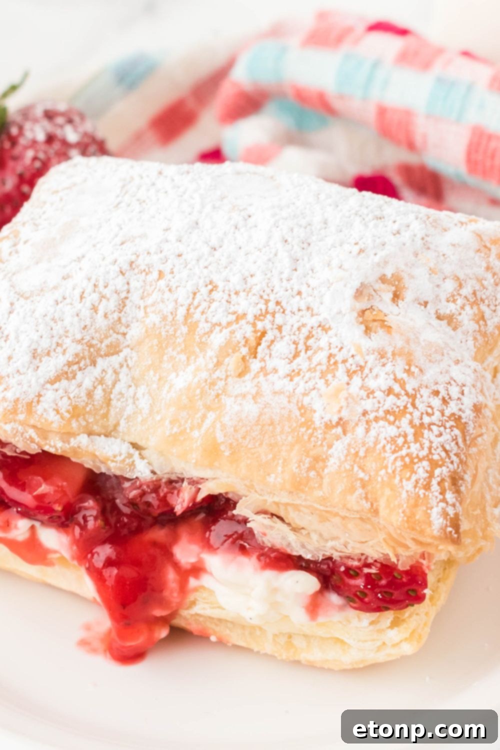 A completed puff pastry dessert, generously topped with fresh strawberries, presented on a plate.