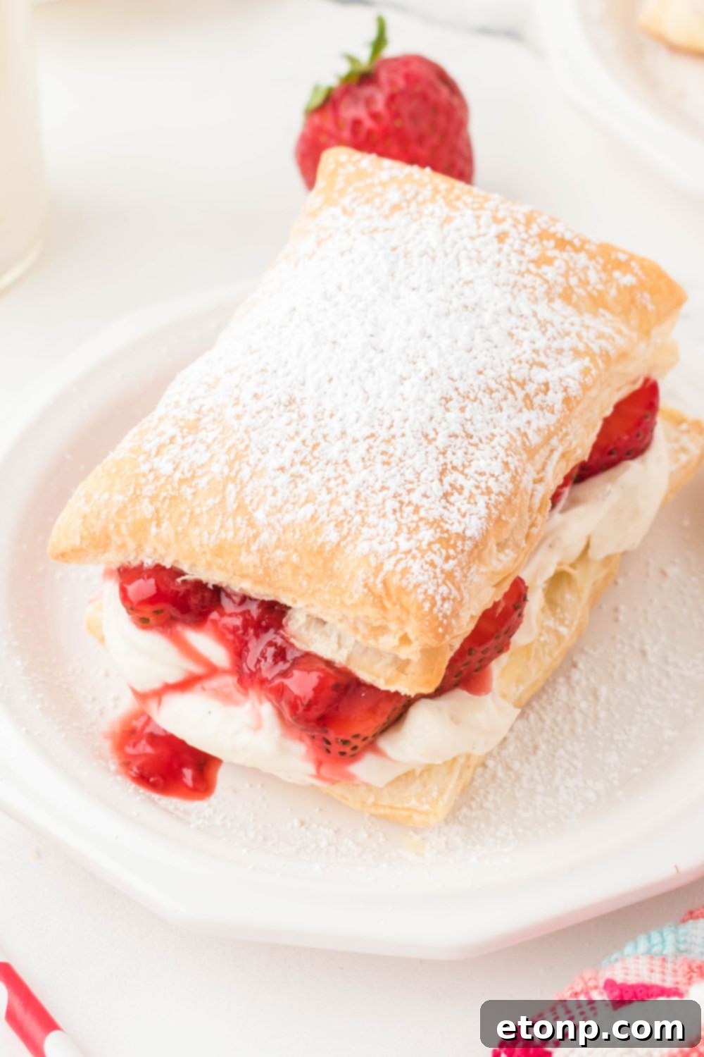 A beautifully presented Strawberry Flaky Puff, with fresh strawberries scattered in the background, creating an inviting scene on a marble counter.