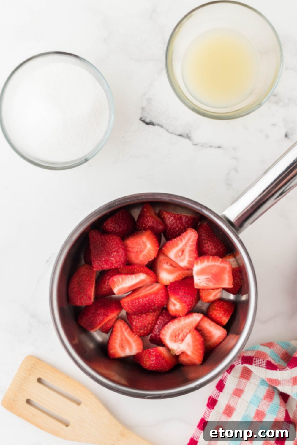 Fresh strawberry slices mixed with sugar and lemon juice in a saucepan, beginning to cook down into a compote.
