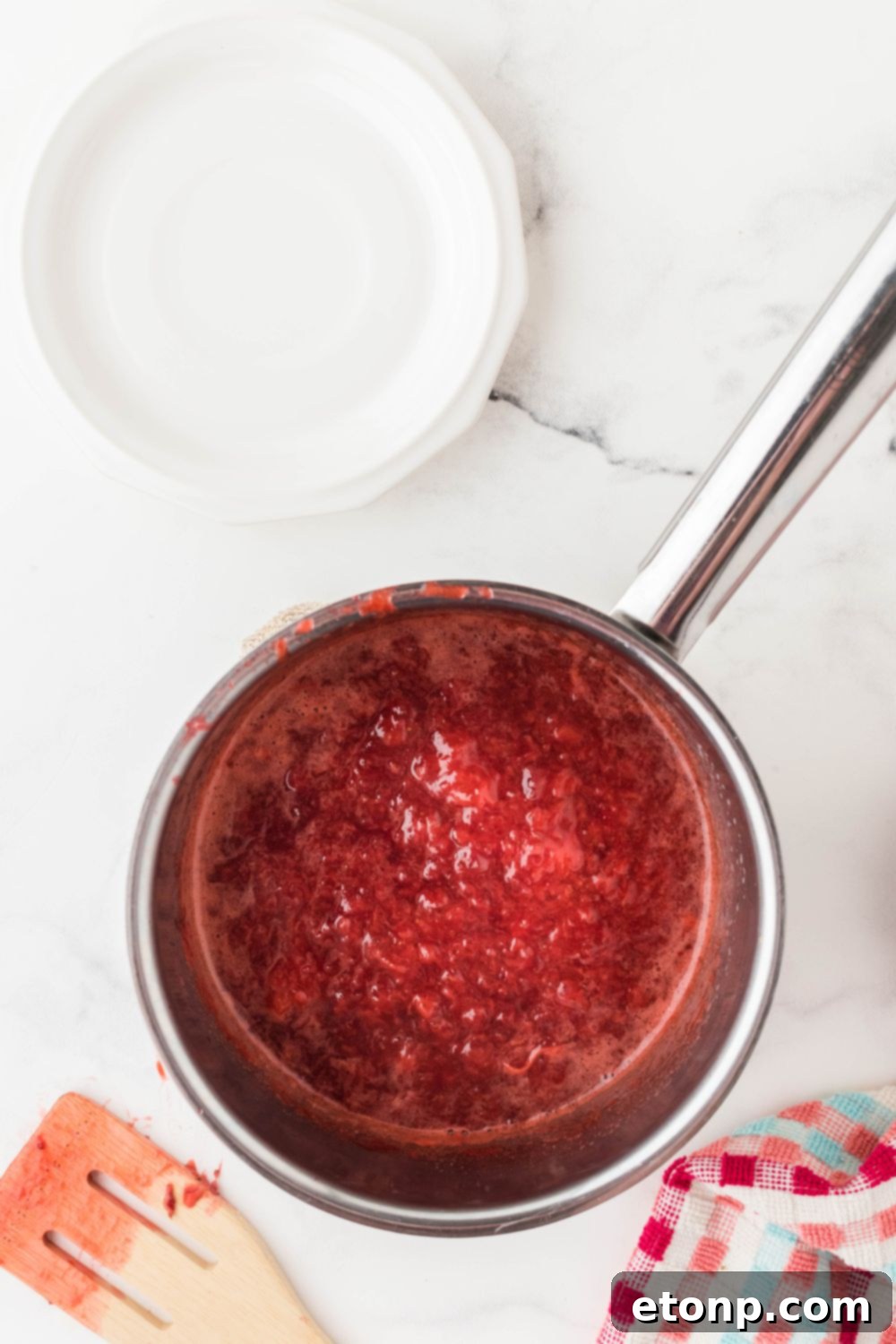 A bubbling strawberry puree thickening in a pan, showcasing its rich red color and syrupy consistency.