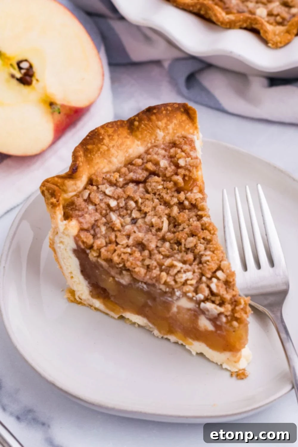 apple crumble cheesecake slice on plate with fork and apple on the side