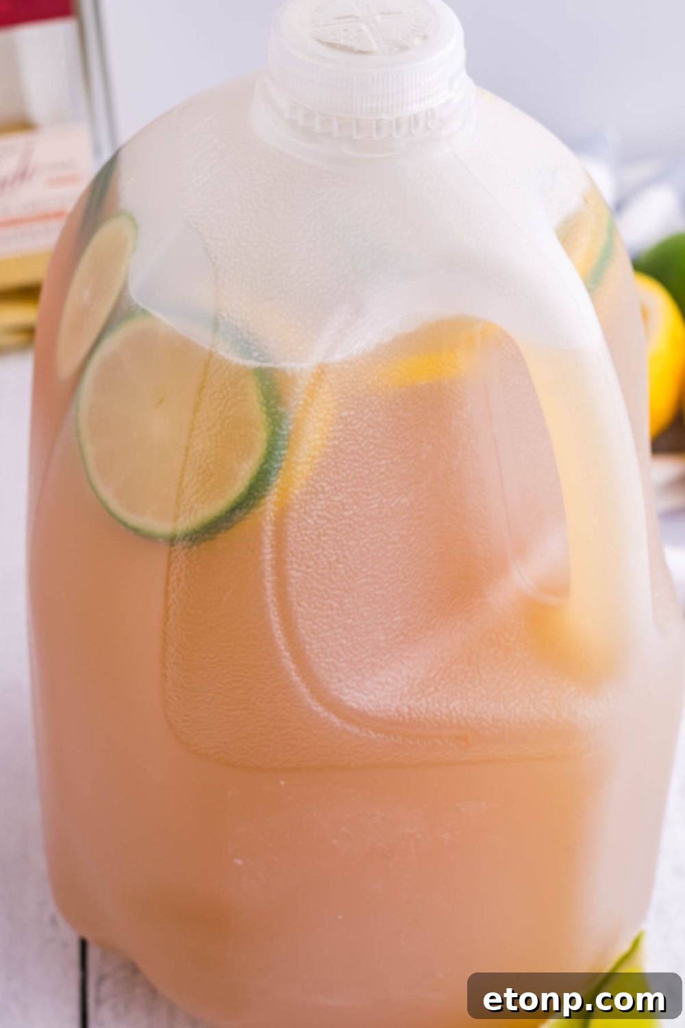 A large jug of Gallon Margarita sitting on a table, surrounded by fresh lime wedges, ready for serving