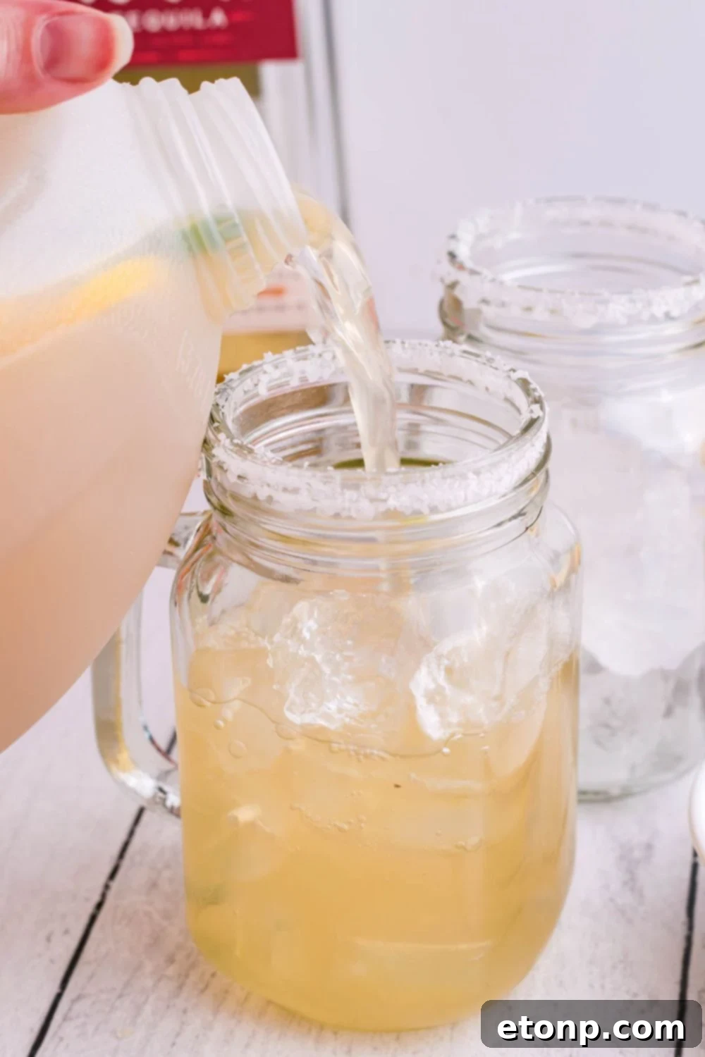 Pouring a freshly mixed margarita from a jug into a mason jar, ready to be enjoyed