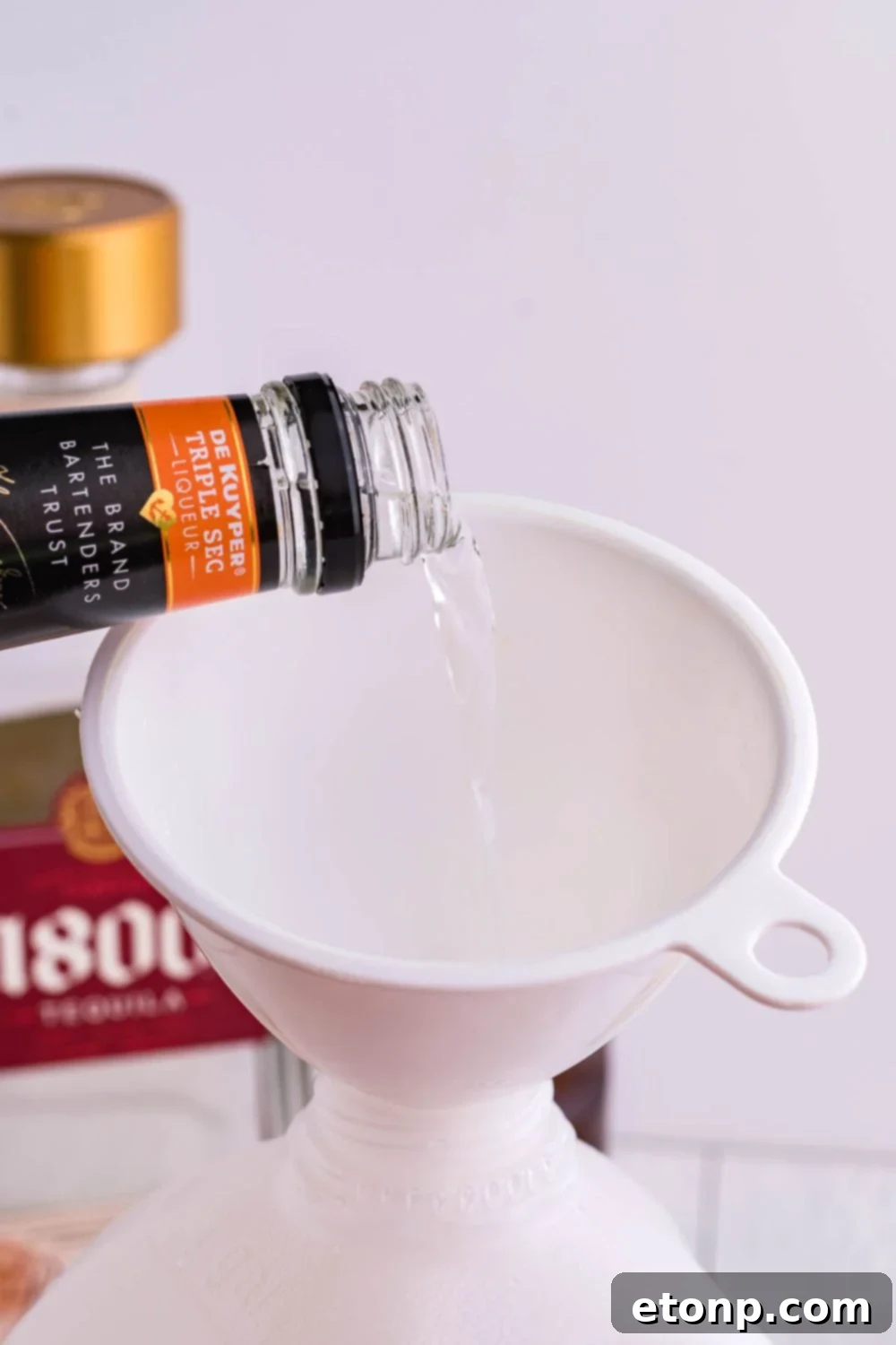 Triple Sec liqueur being poured into a funnel inserted into a large jug
