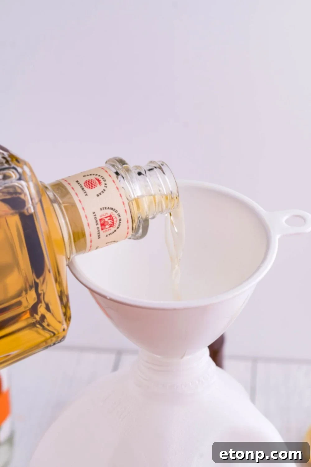 Tequila being poured through a funnel into a jug for a batch cocktail