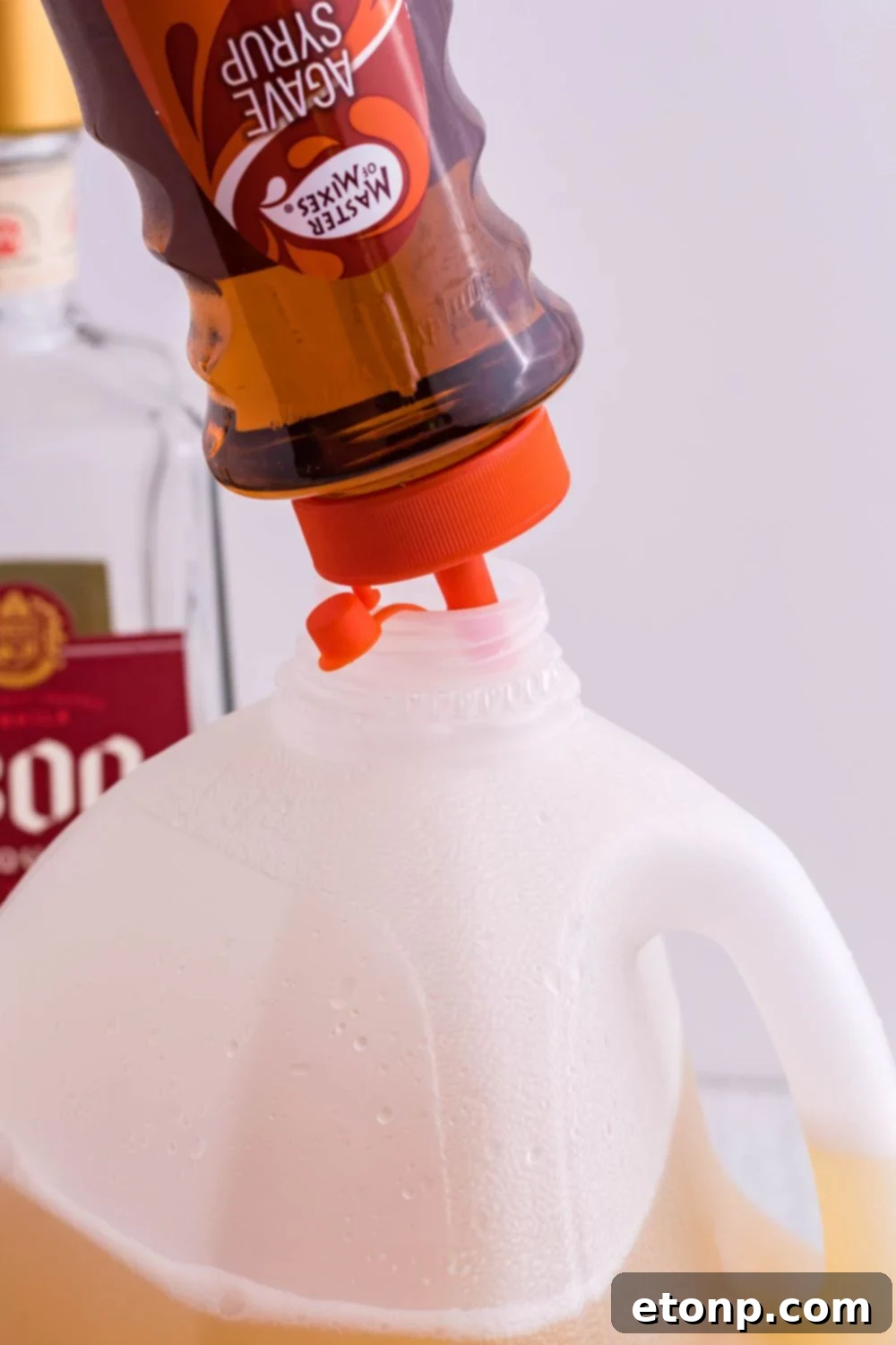 Agave syrup, labeled as simple syrup, being poured into a milk jug for a margarita mix