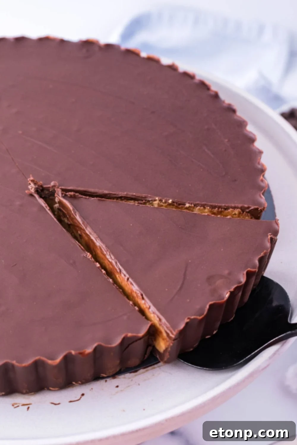 A Giant Reese's Cup Pie with a slice being removed by a spatula, highlighting its rich layers