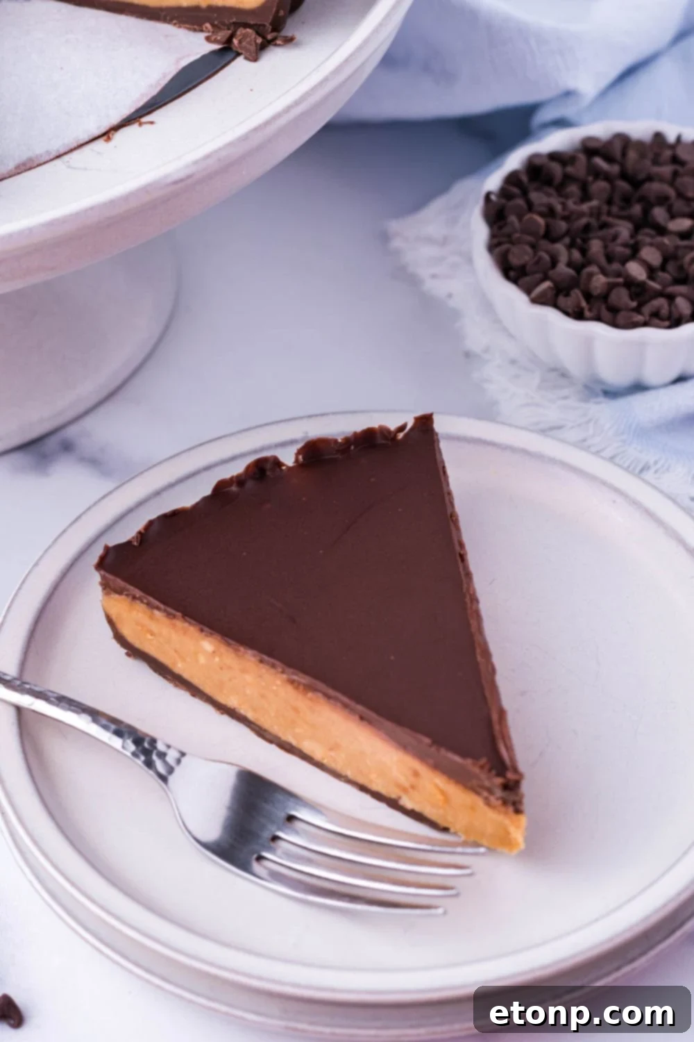 A slice of Giant Reese's Cup Pie on a white plate with a fork next to it, inviting a bite