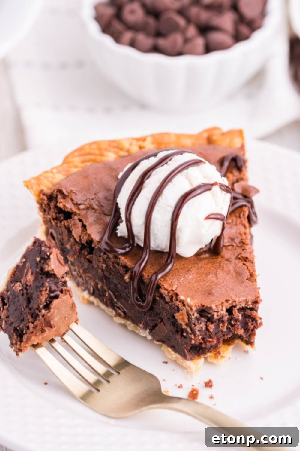 A slice of brownie fudge pie on a plate with a bite taken out by a fork, highlighting its rich, dark interior.