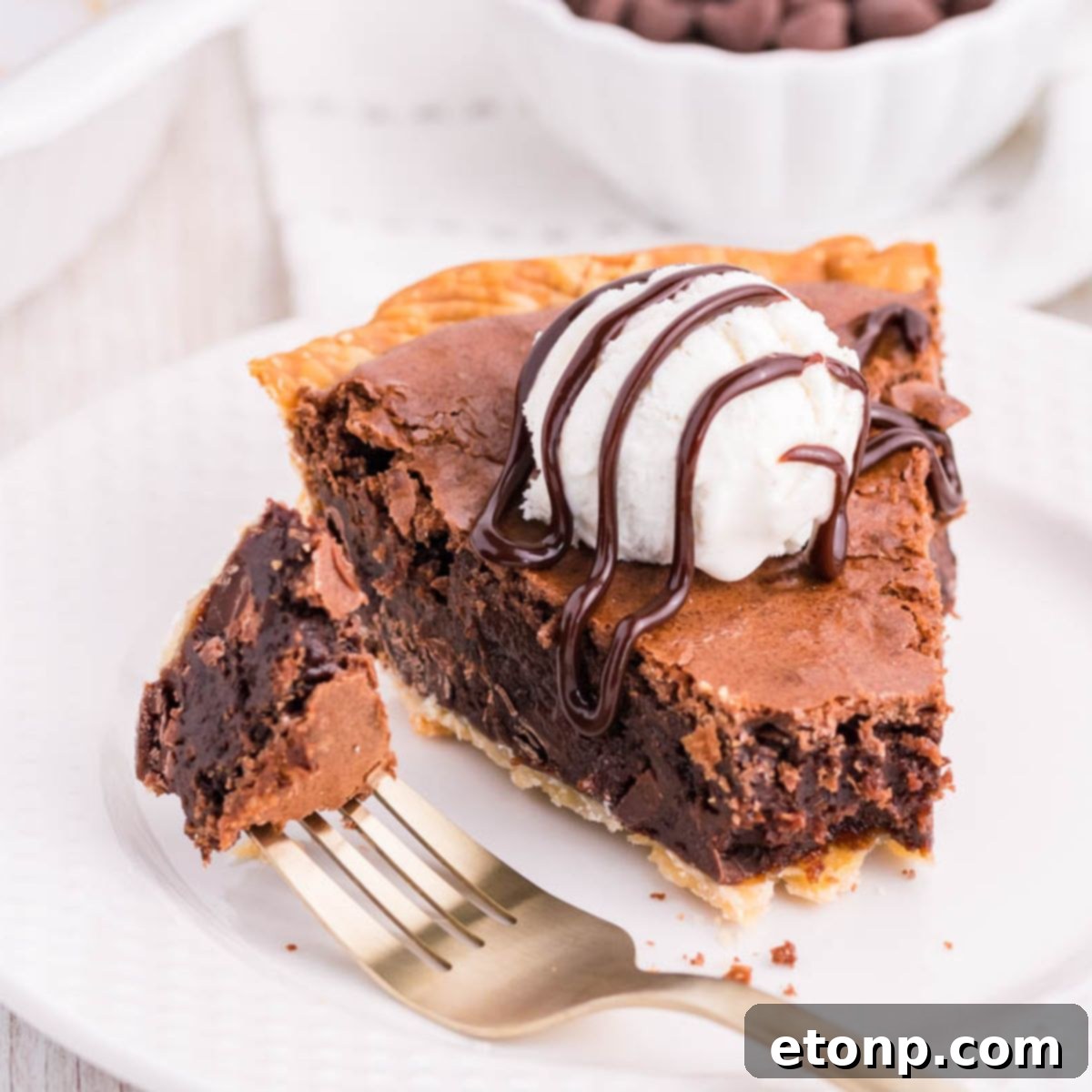 A slice of Fudge Brownie Pie on a white plate with a fork, showing its gooey center and crisp crust.