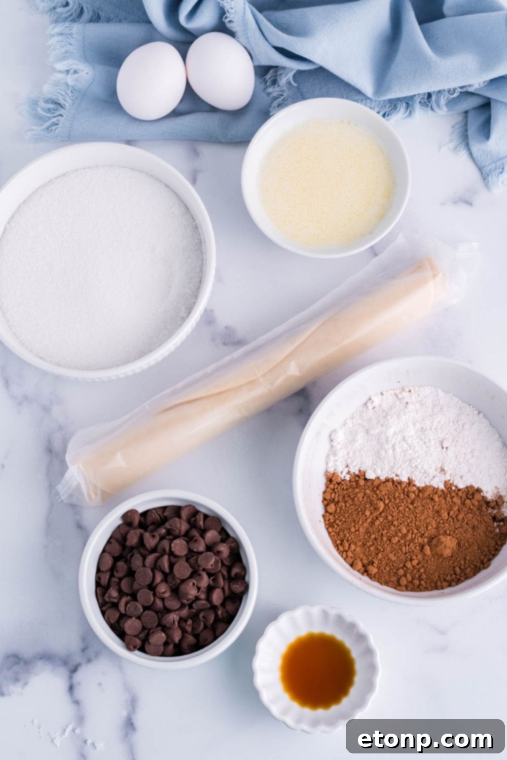 Ingredients for fudge brownie pie laid out on a table, including butter, sugar, eggs, cocoa powder, and chocolate chips.