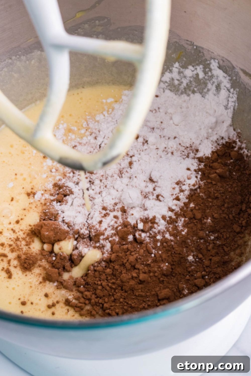 A stand mixer with brownie batter ingredients in a bowl, being mixed.