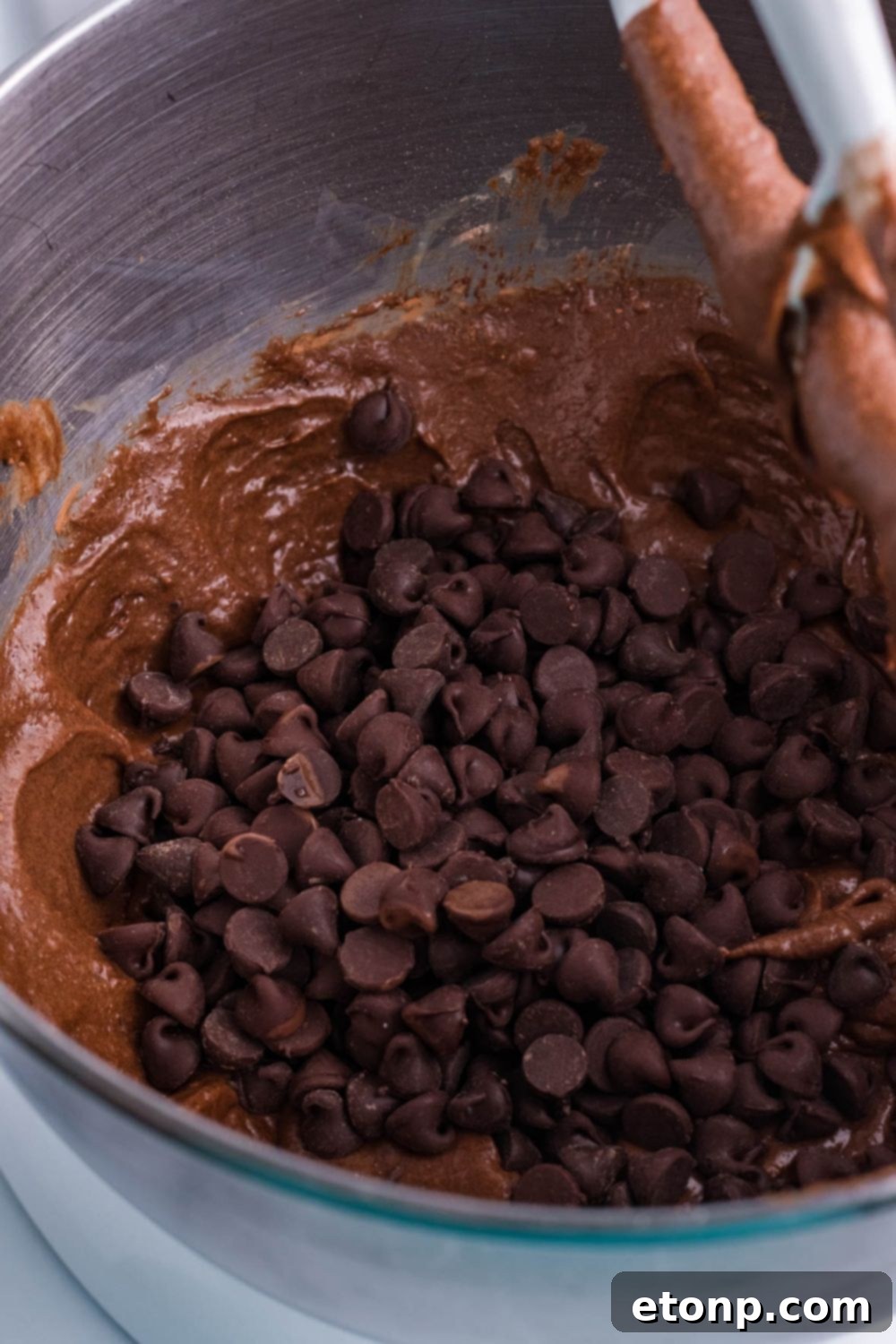 Chocolate chips generously sprinkled on top of the brownie pie batter in a bowl, ready to be folded in.