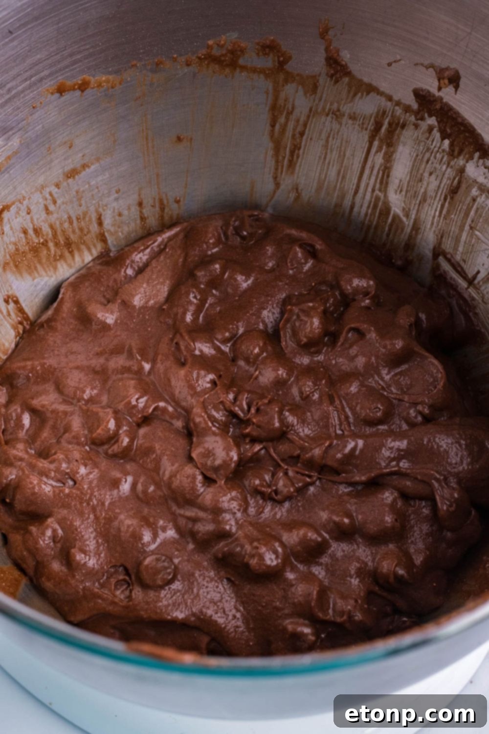 Brownie batter with chocolate chips being mixed in a stand mixer, showcasing its rich texture.