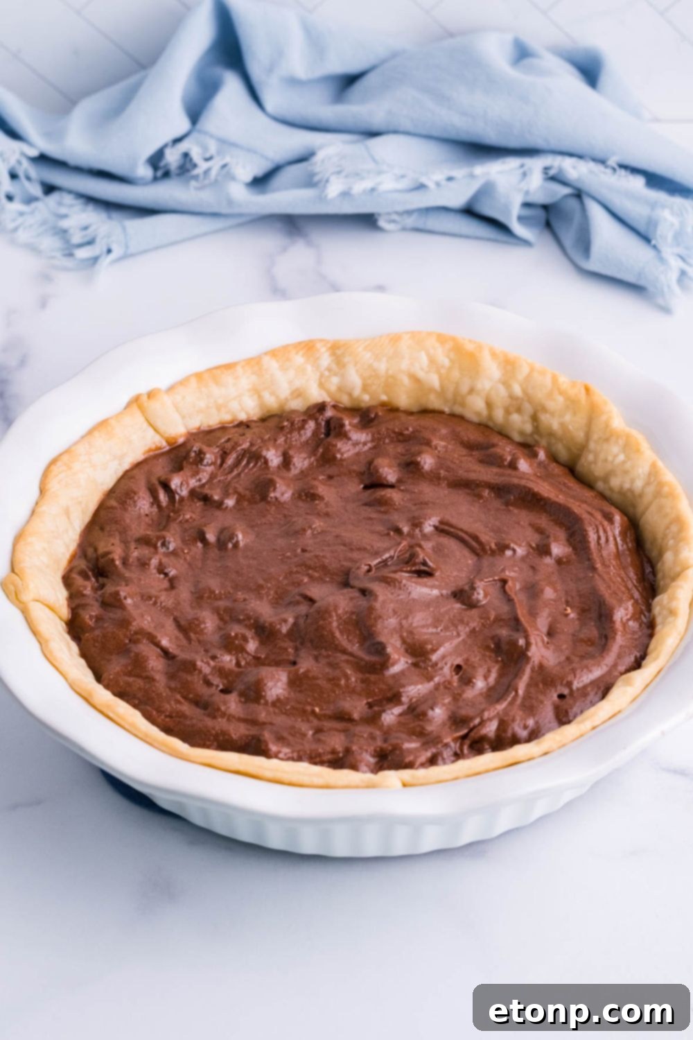Smooth, chocolatey brownie batter poured into a pie crust in a pan on a table, ready for baking.