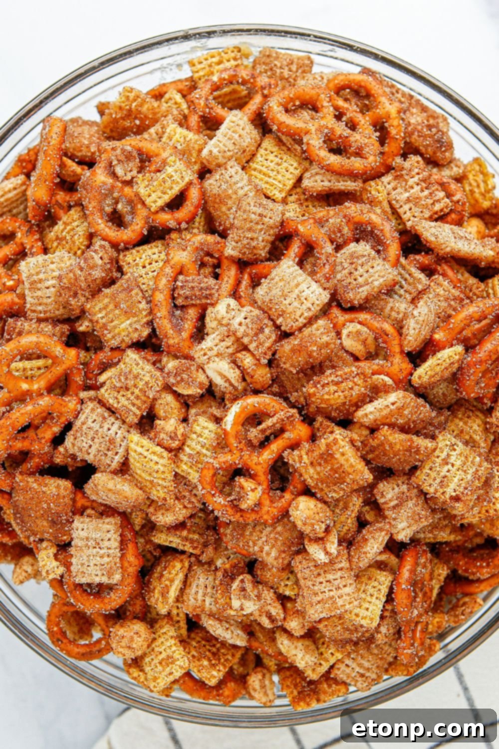 A beautifully presented Churro Chex Mix in a clear glass bowl, resting on a table with a soft towel underneath.