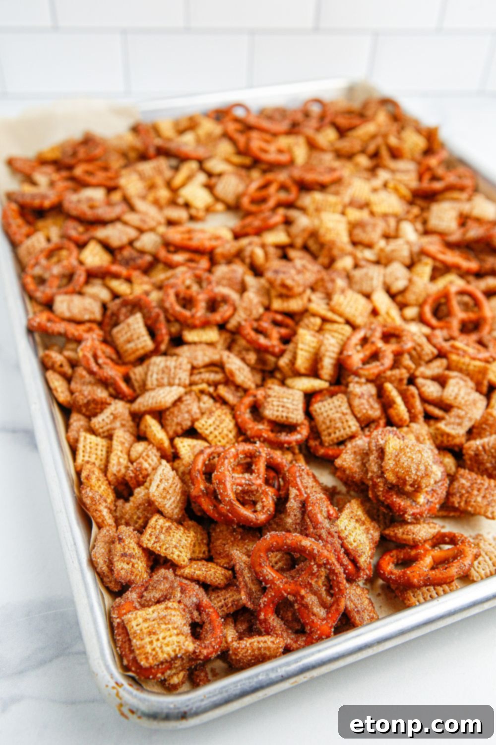Churro Chex Mix spread evenly on a cookie sheet, ready for baking or cooling, set on a wooden table.