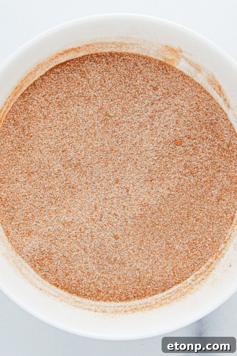 A small glass bowl filled with the perfectly blended cinnamon and sugar mixture, ready for coating.