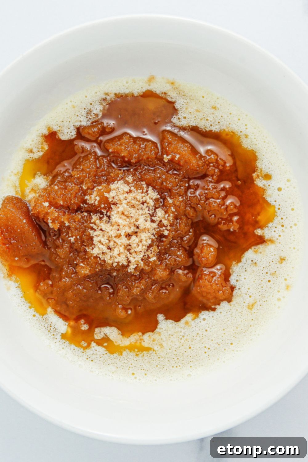 A mixing bowl holding a warm, rich mixture of melted butter and brown sugar, forming the base of the glaze.