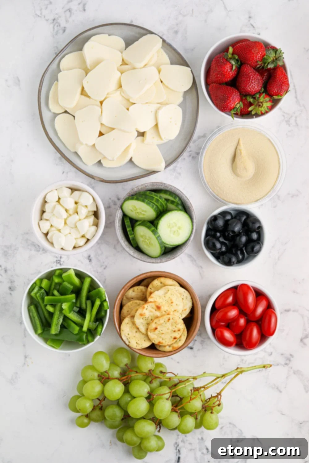 All the fresh ingredients for the Santa Snack Tray laid out on a table before assembly, including fruits, vegetables, cheeses, and hummus.