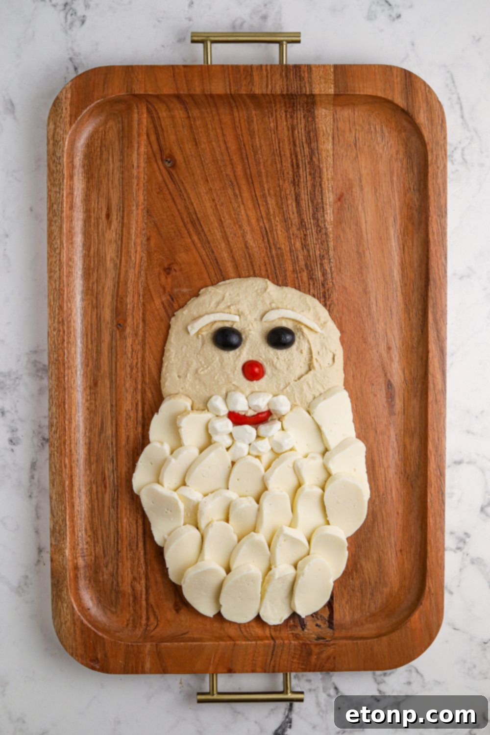 Partially shaped Santa snack board, showing the initial placement of hummus, eyes, and nose.
