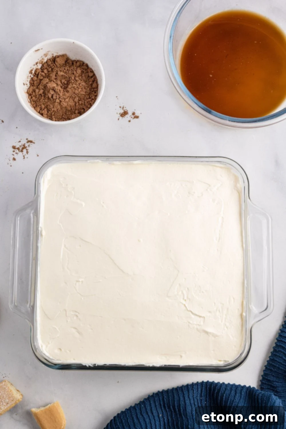 A generous layer of the creamy mascarpone cheese mixture being spread evenly over the base of coffee-soaked ladyfingers in the pan.