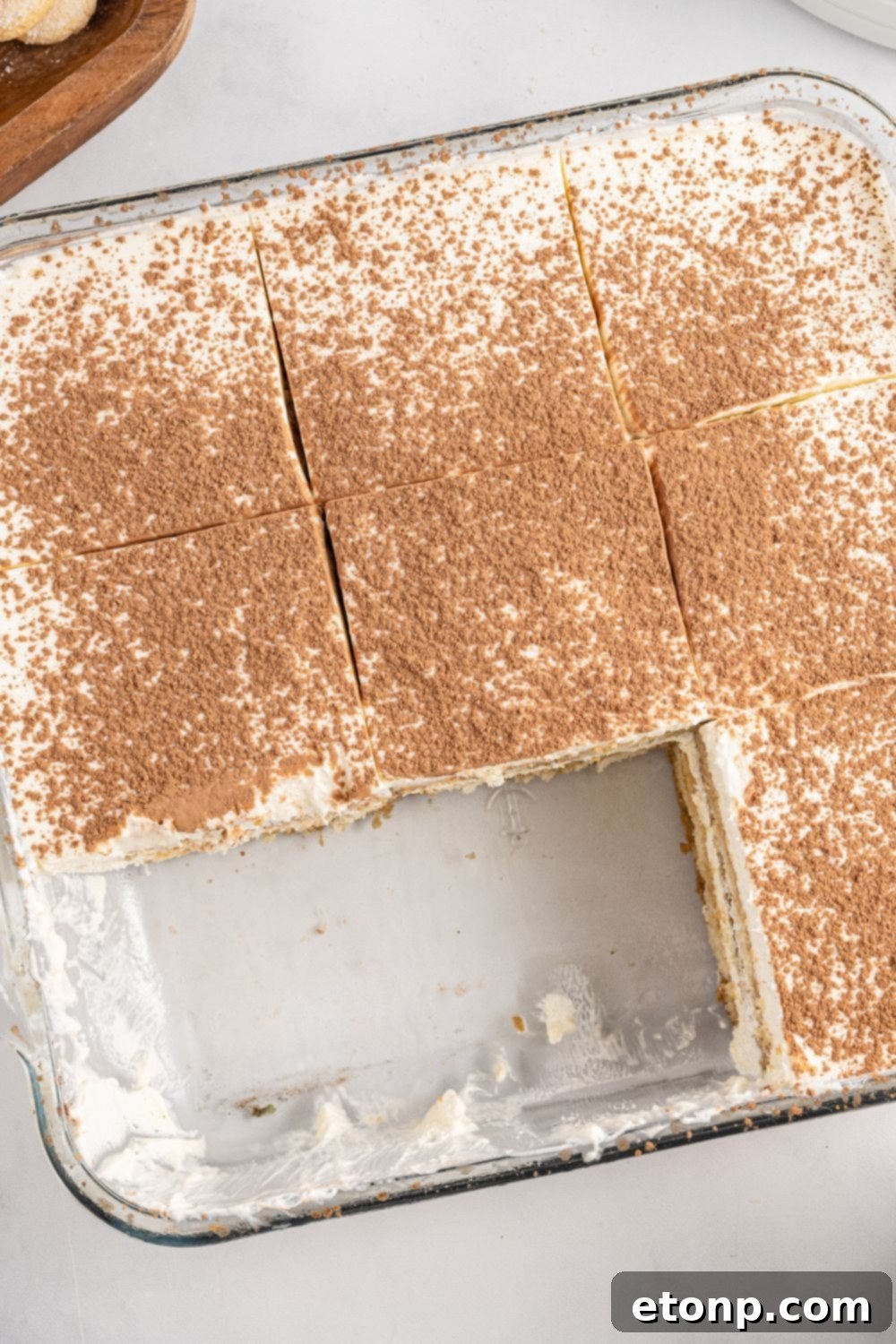 A square pan of tiramisu with several slices already removed, showing the clean, distinct layers of the dessert.