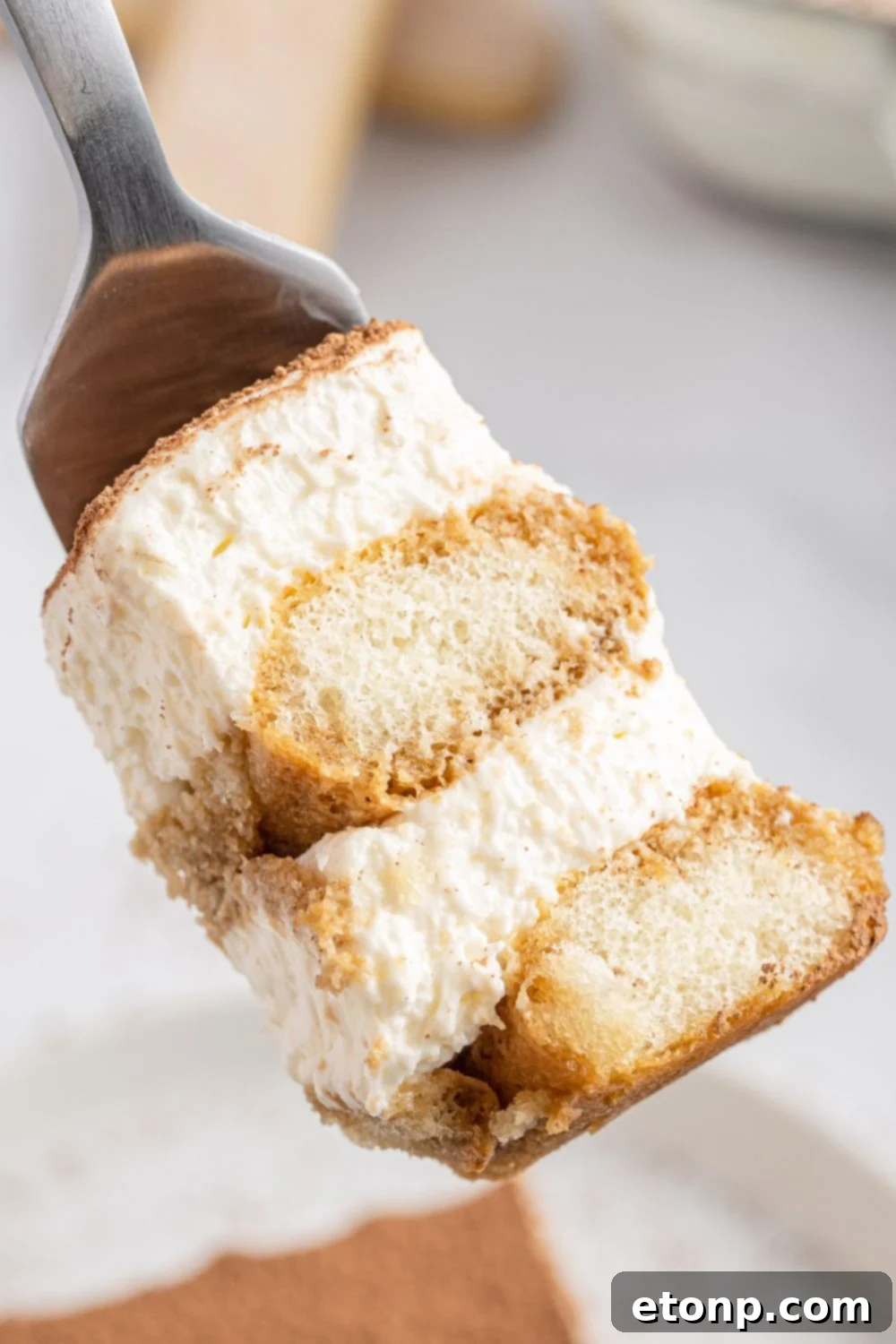 A perfect bite of tiramisu captured on a fork, held above a white plate, highlighting its smooth texture and cocoa dusting.