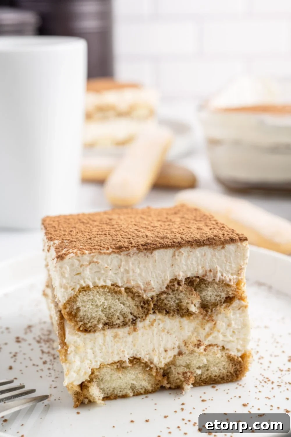 A beautifully crafted cafe tiramisu presented on a white plate, adorned with a delicate dusting of cocoa powder.