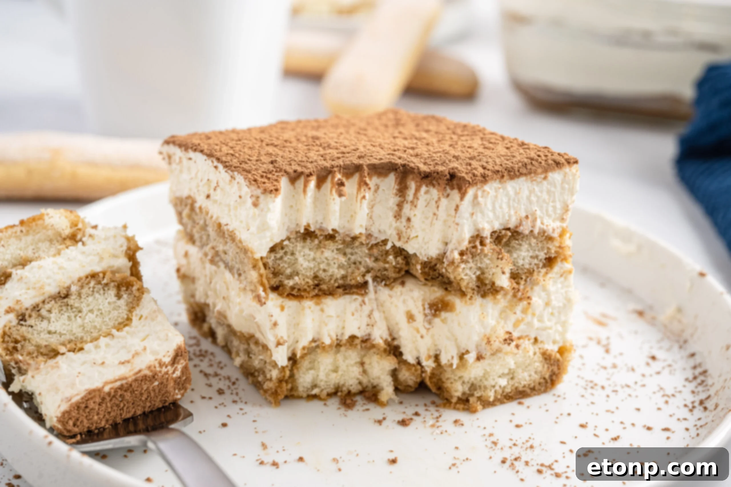 A pristine slice of tiramisu resting on a white plate, with a small portion gently removed, highlighting its beautiful layers and inviting texture.