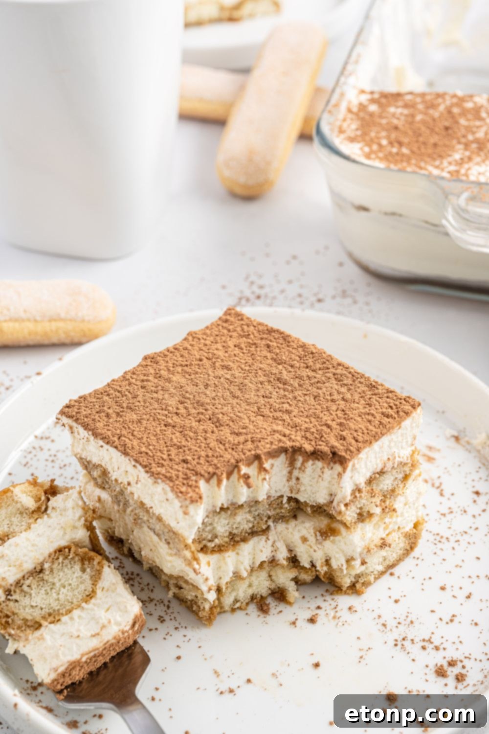 A fork holding a perfect bite of tiramisu, poised above a plate, showcasing the creamy filling and a hint of cocoa dusting.
