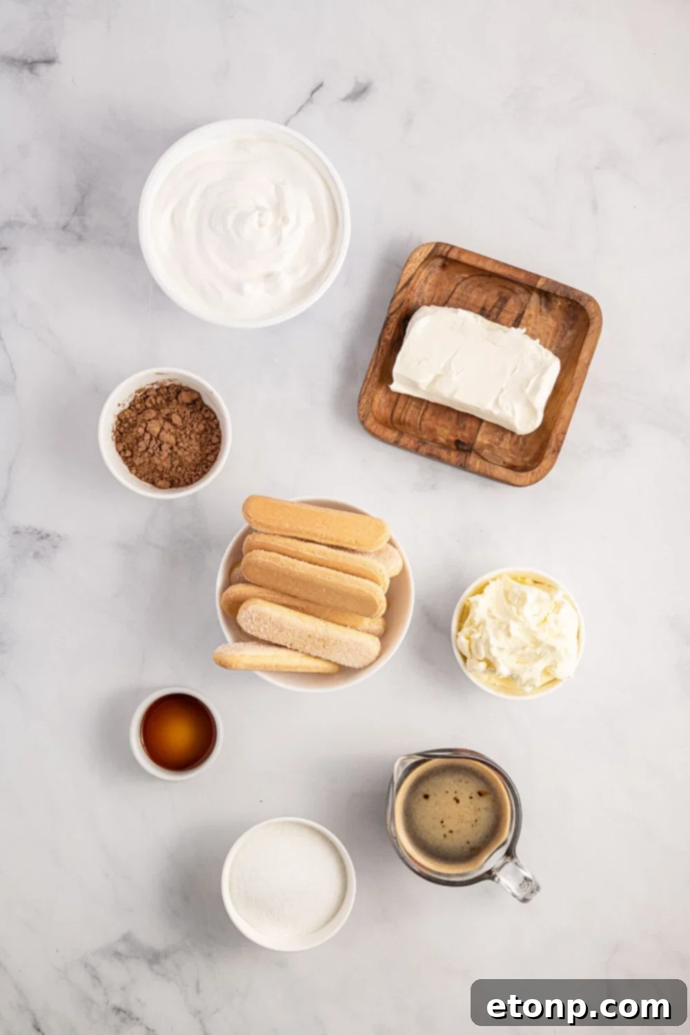 A rustic wooden table displaying all the essential ingredients for making tiramisu, including mascarpone, ladyfingers, coffee, and cocoa powder, artfully arranged for a visually appealing presentation.