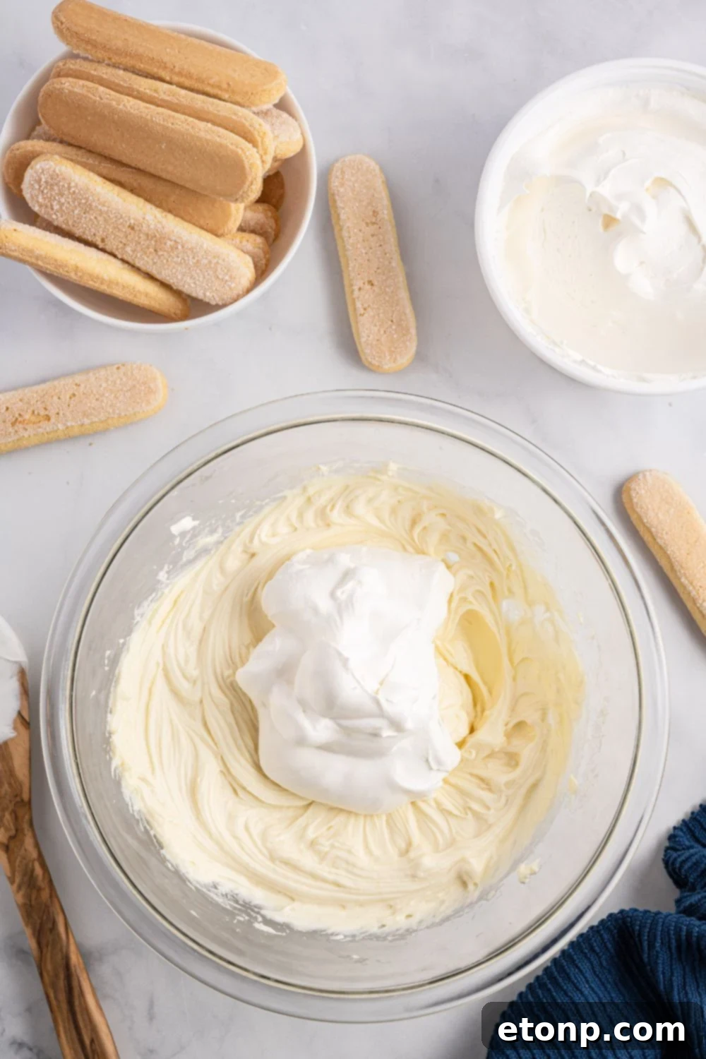 Ingredients for the rich and creamy base of tiramisu, including mascarpone and cream cheese, mixed together in a clear glass bowl, ready for the next step.