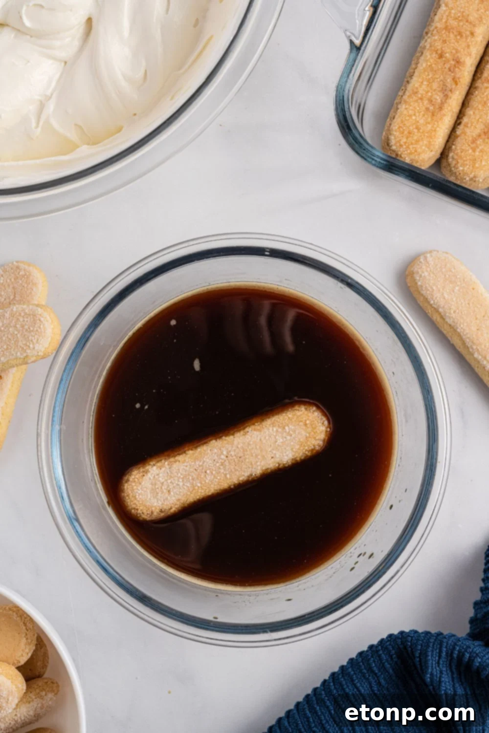 A ladyfinger cookie being quickly dipped into a shallow bowl of dark, freshly brewed coffee, ready to absorb the rich flavor.