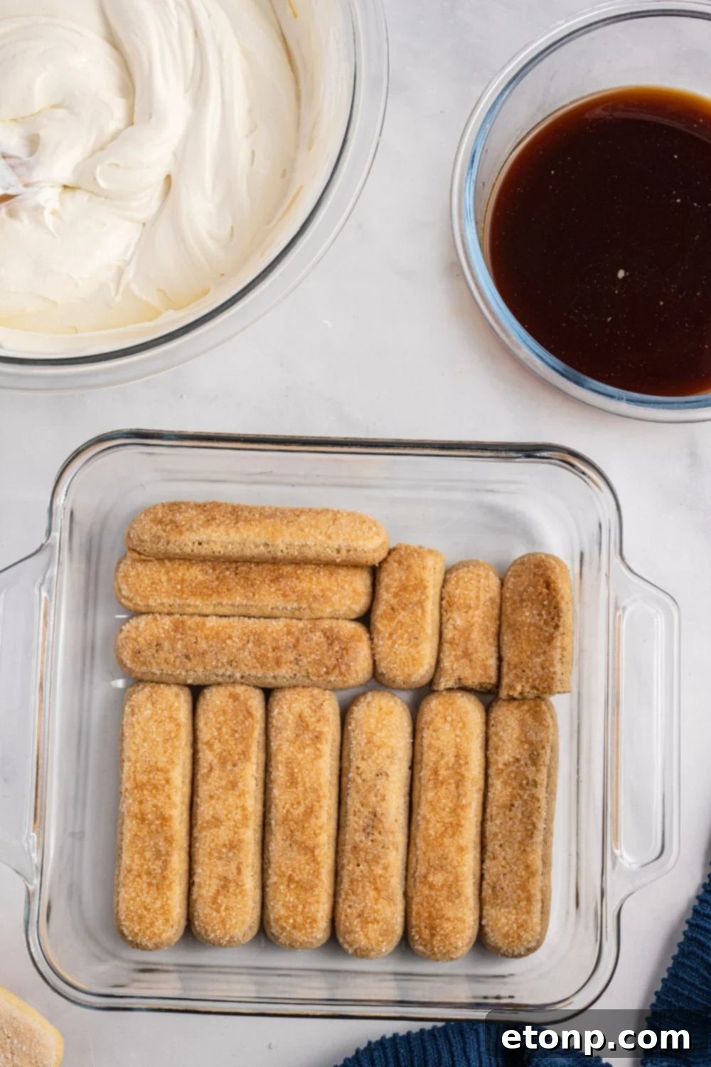 Several coffee-dipped ladyfingers neatly arranged in a baking pan, forming the first layer of the tiramisu dessert.