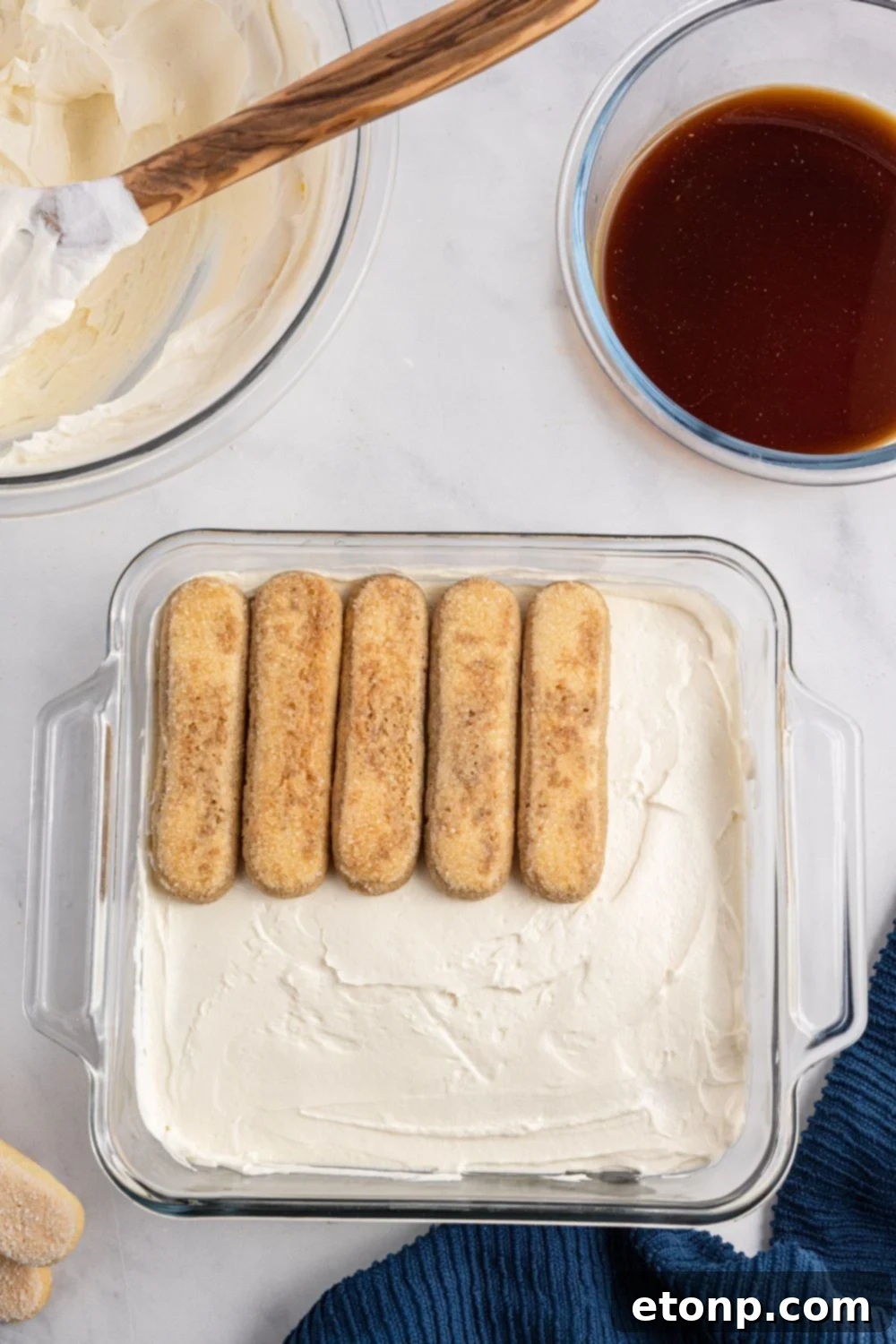 More ladyfingers being carefully placed in the baking pan, filling in gaps to create a solid, even base layer for the tiramisu.