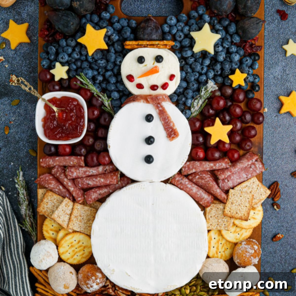 Whimsical Snowman Snack Board 2 Overhead view of a beautifully arranged Snowman Charcuterie Board on a rustic table, laden with festive snacks.