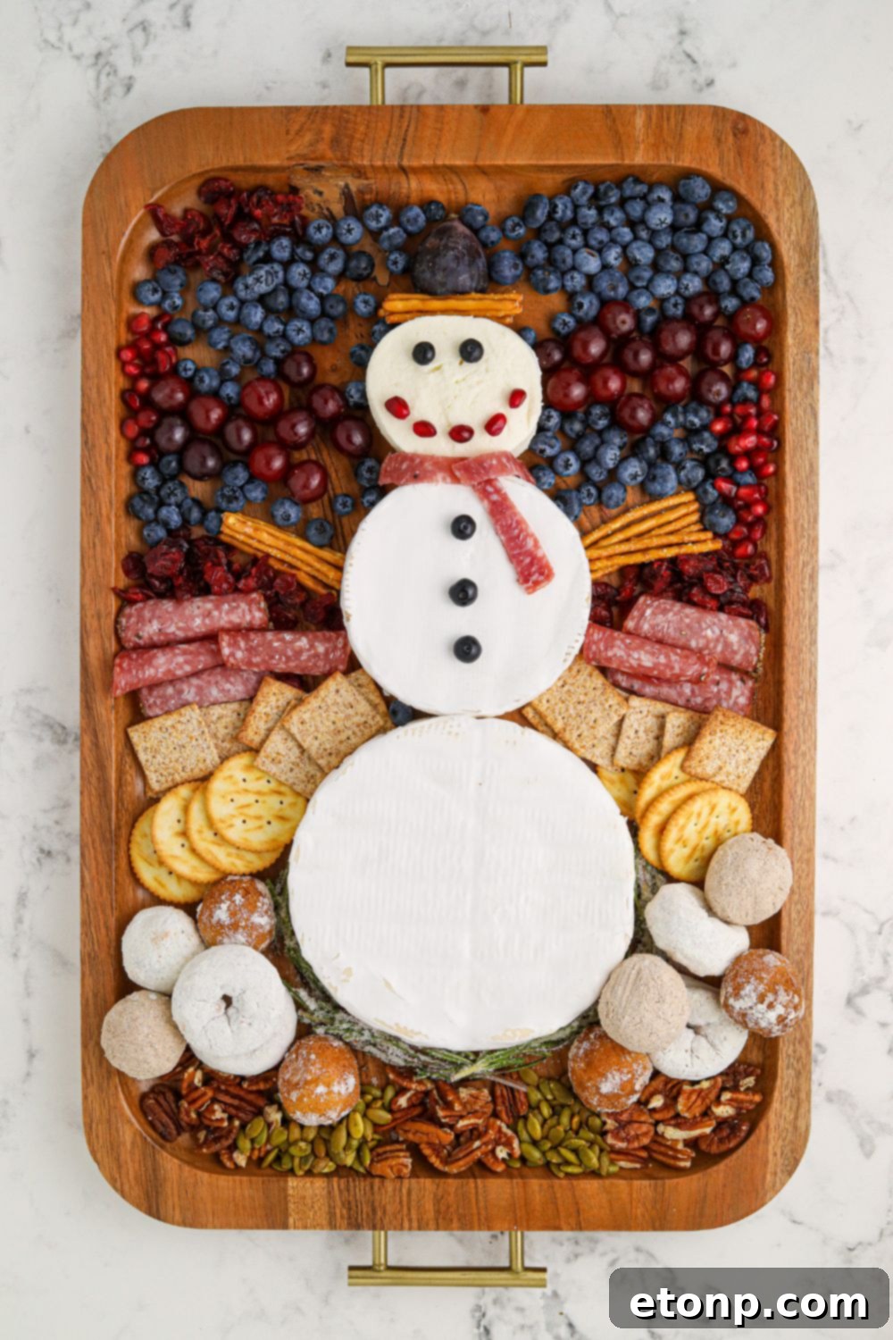 Whimsical Snowman Snack Board 8 The process of assembling the Snowman Charcuterie Board with various snacks and fruits.