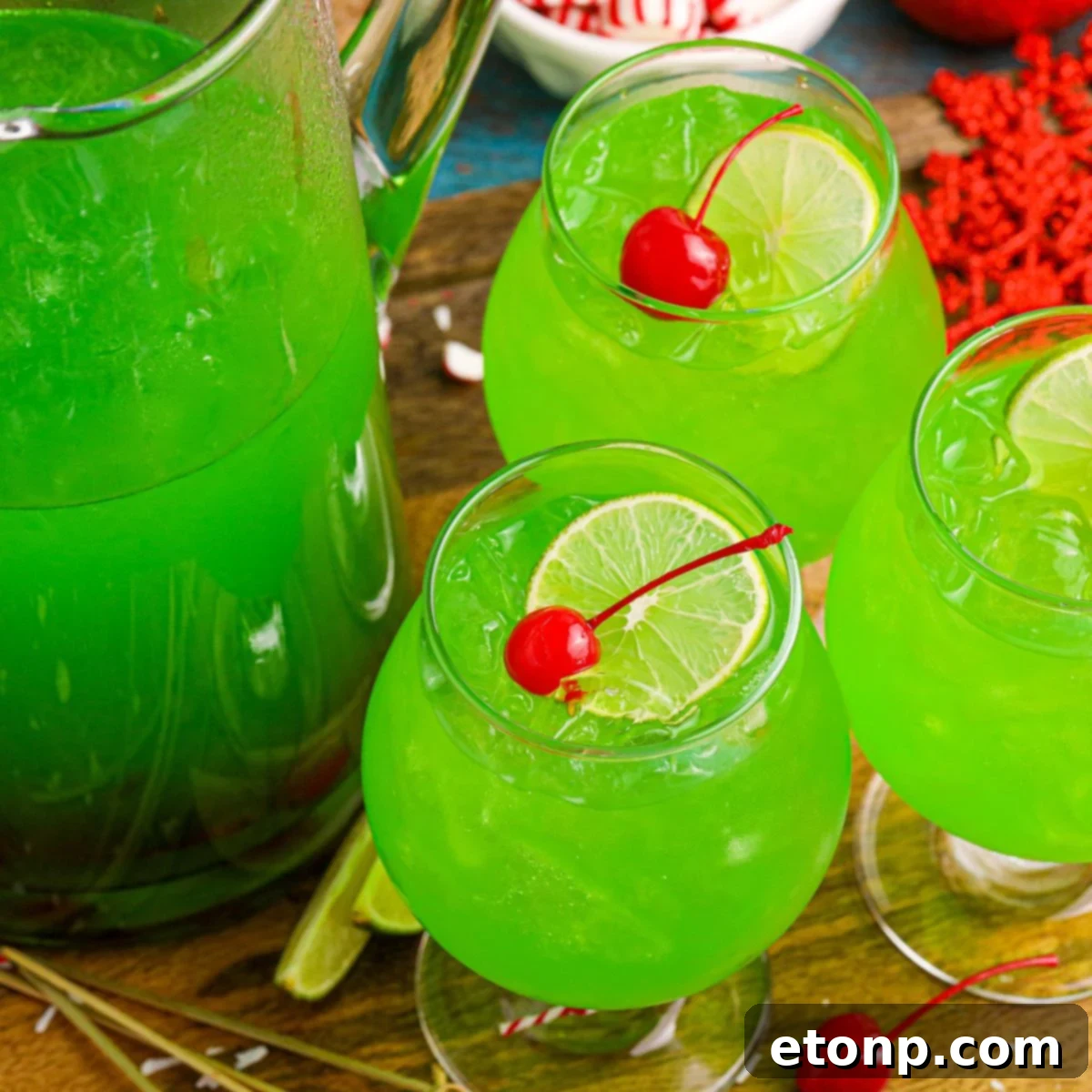 Close-up of a glass of Grinch Punch, garnished with a cherry and a lime wedge, on a festive holiday table.