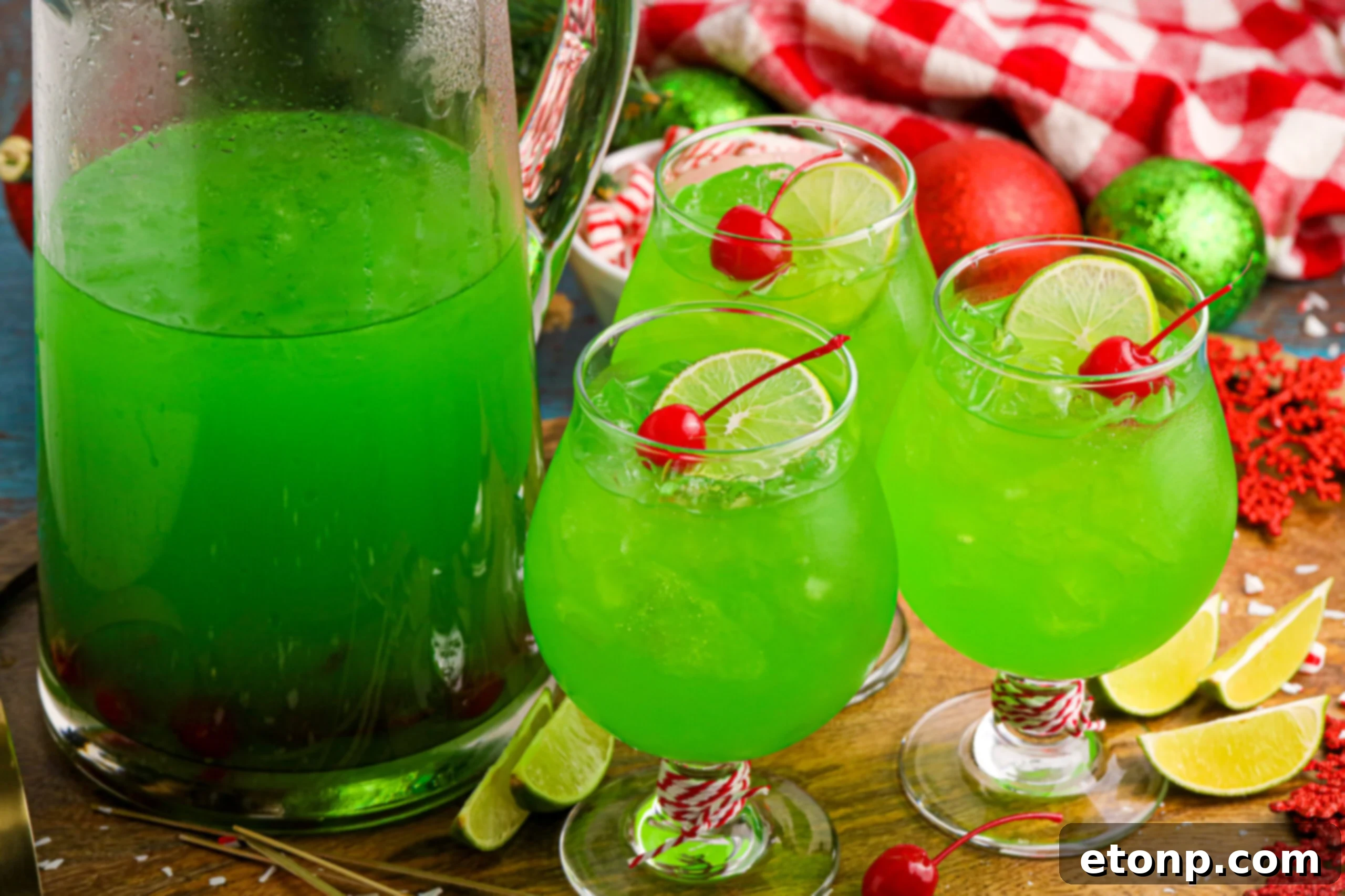 A pitcher of Grinch Punch surrounded by individual glasses, each garnished with a cherry and lime slice, ready for serving.