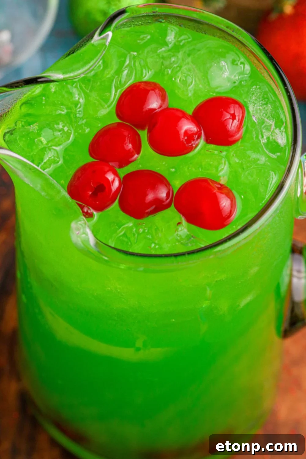 A pitcher of bright green Grinch Punch, with red maraschino cherries floating on top, ready to be served.