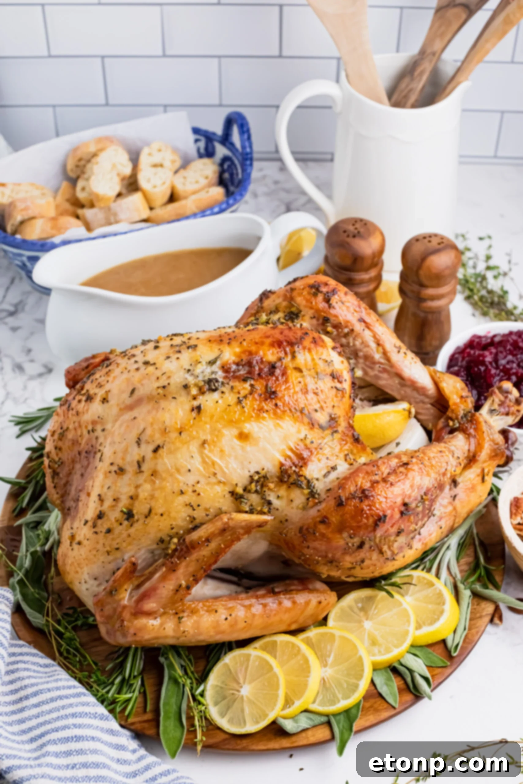 Roasted turkey on a wooden cutting board with gravy in a white bowl and cranberry sauce in another bowl in the background