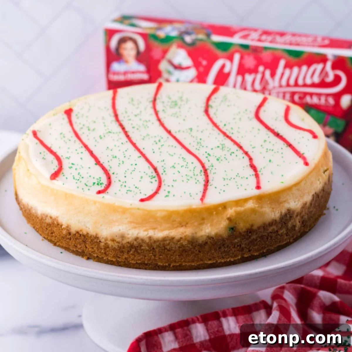 A stunning Little Debbie Christmas Tree Cheesecake adorned with red icing and green sprinkles, presented on a festive cake platter, ready to be enjoyed.