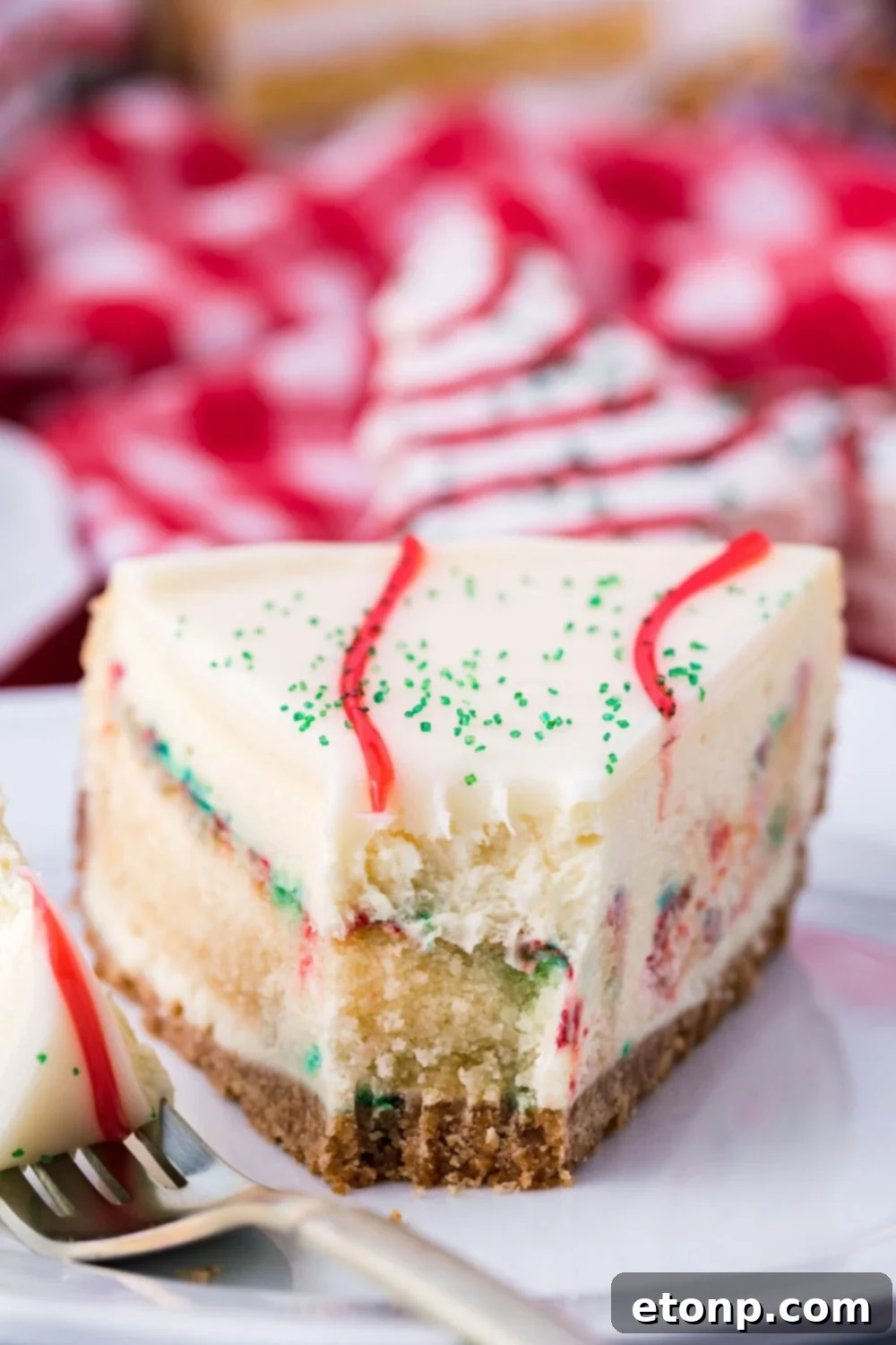 A close-up of a slice of Little Debbie Christmas Tree Cheesecake on a plate, with a bite taken out, highlighting the moist cake pieces within the creamy cheesecake.