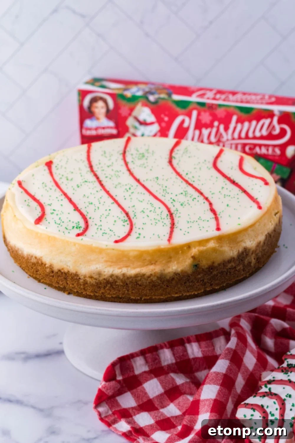 A whole Little Debbie Christmas Tree Cheesecake on a pristine white cake platter, prominently displayed on a wooden table, awaiting its first slice.